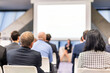 © kasto - Business and entrepreneurship symposium. Female speaker giving a talk at business meeting. Audience in conference hall. Rear view of unrecognized participant in audience.