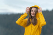 Portrait of young woman in yellow raincoat outside. Girl on hike in autumn look at camera.