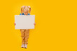 Cute little blonde girl with two ponytails with white sheet of paper. Isolated on yellow background. Copy space.