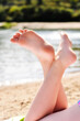Happy kid lying barefoot on the beach enjoying the sun. Closeup of legs pointing up. Tropical landscape of the sand and water.