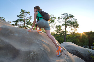 Wall Mural - Sportive woman climbing alone on hillside rocky trail. Female hiker overcoming difficult cliff on wilderness path. Active lifestyle concept