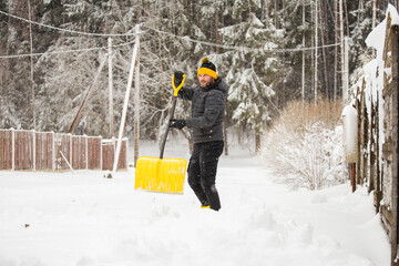 Deep drifts of snow after a heavy storm - an adult man clears the paths from snow with a shovel - digging a car out of a snowdrift