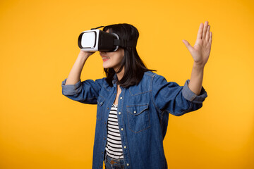 Poster - Young asian woman happy success wearing virtual reality headset game entertainment isolated on yellow background. Winner of cyber future video game concept.