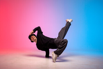 young guy dancer in black clothes break dancing in neon lighting, man performs hip hop movement in red blue club