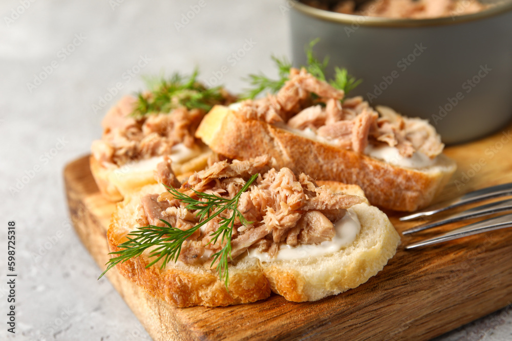 Board with delicious tuna bruschettas and tin can on grey table