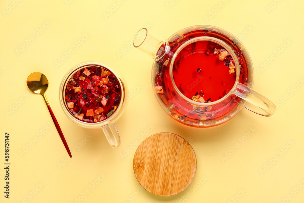Transparent teapot with cup of fruit tea on yellow background