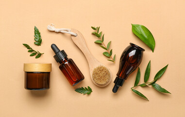 Bottles of cosmetic oil with plant leaves and brush on beige background