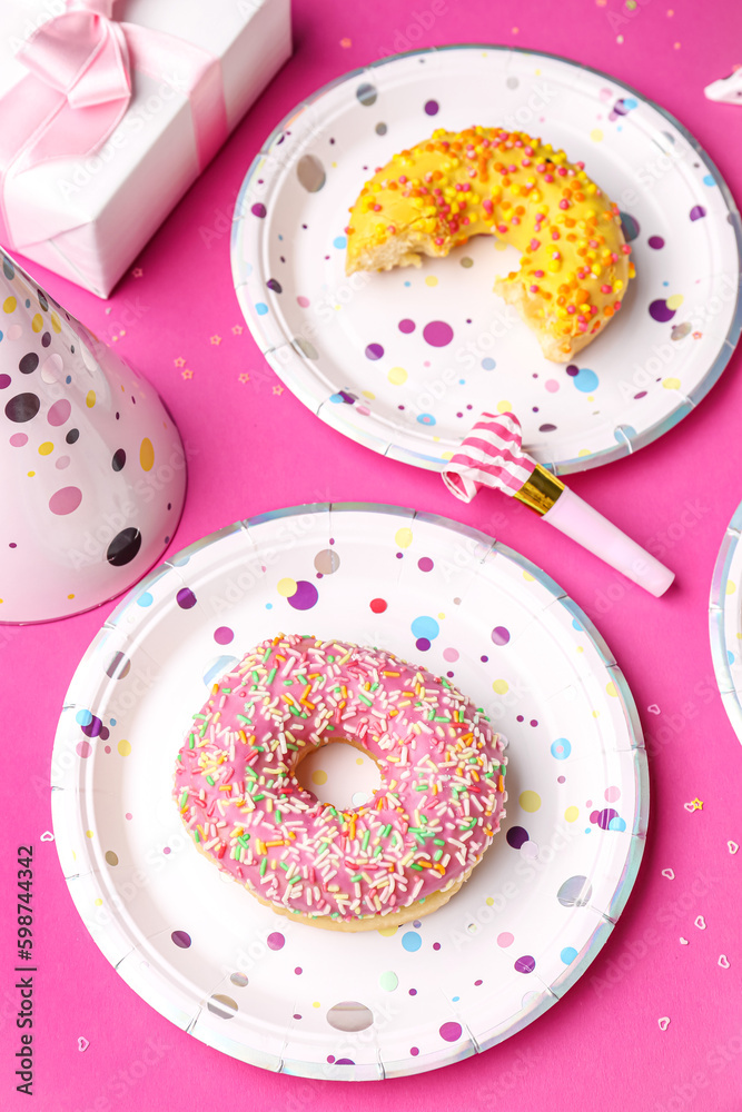 Paper disposable plates with donuts and party blower on pink background, closeup