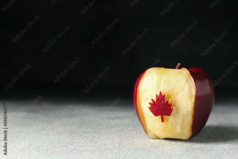 Apple with cut maple leaf on black and white background. Canadian flag concept
