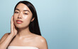 © Liubov Levytska - Women beauty. Young asian woman with perfect skin, glowing face after nourishing cream, touching her cheek, applying moisturizer, spf protection, blue background