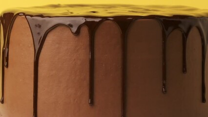 Wall Mural - Chocolate drips of melted dark chocolate on the brown cream cheese frosted cake. Close up. Textured background. Cake rotating on the yellow background