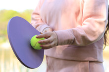 Women's Hands With A Wooden Racket And A Green Ball Close-up. Outdoor Sport Leisure Activity