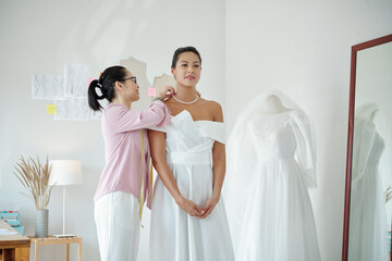 Wall Mural - Smiling bridal salon assistant helping client to wear pearl necklace