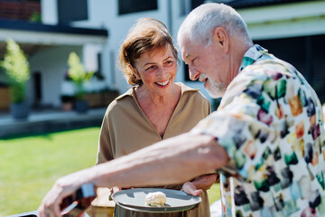 Wall Mural - Senior man grilled outdoor at garden, giving his wife hamburger.