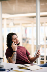 Aufkleber - Im going to send you the updates right now. a young businessman talking on a cellphone while using a digital tablet in an office.