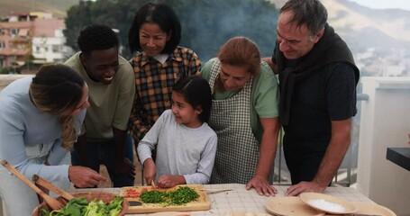 Wall Mural - Multiracial friends having fun preparing food with girl during weekend day - Multi generational people doing barbecue at home's rooftop - Latin child cutting carrots