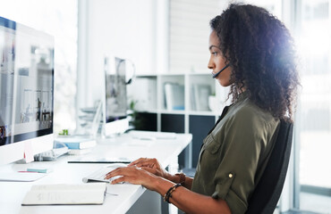 Poster - Focused on finding a solution. a young woman using a headset and computer in a modern office.