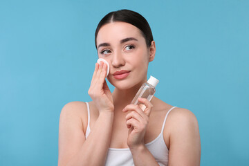 Beautiful woman removing makeup with cotton pad on light blue background