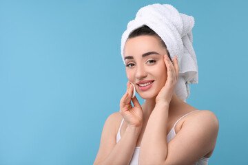 Wall Mural - Beautiful woman in terry towel removing makeup with cotton pad on light blue background, space for text