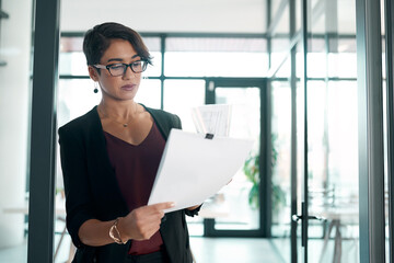 Poster - Hmm, theres definitely room for improvement. an attractive young businesswoman standing alone in the office and reading paperwork.