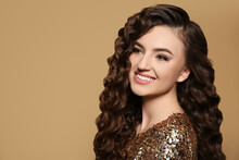 Beautiful Young Woman With Long Curly Brown Hair In Golden Sequin Dress On Beige Background, Space For Text