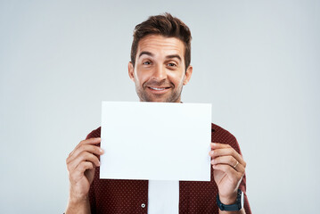 Poster - I just made this for you. Portrait of a cheerful young man holding and displaying a poster while standing against a grey background.