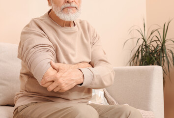 Wall Mural - Senior man suffering from pain in his hand at home, closeup. Arthritis symptoms