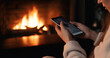 © jr-art - a woman is doing something on her smartphone in front of a burning fireplace. Generative AI