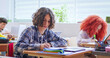 © ihorvsn - Serious preteen students listening to teacher and writing exercises in notebook during lesson in primary school. Thoughtful boy with curly hair using digital tablet on desk.