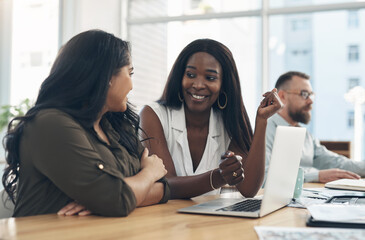 Aufkleber - Women are the backbone of a business. two young businesswomen sitting together and using a laptop while their colleagues work in the background.