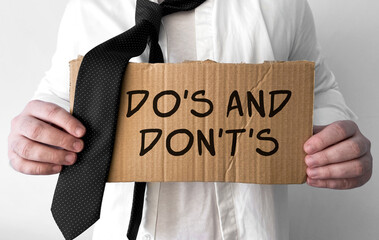 Poster - A disheveled business man holds up a cardboard sign with the words Dos and donts
