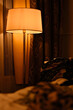 Hotel room with a romantic feeling. Beautiful lampshade giving warm yellow light. Gorgeous brown curtains in the background with pretty patterns. Foreground is blurry.