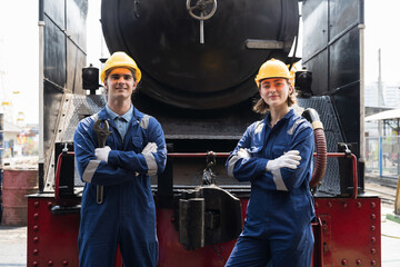 Portrait of male and female engineer worker working, standing with crossed arms, wearing safety uniform, helmet, gloves in locomotive garage. Group of railway engineer repair railhead engine in garage