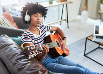 Poster - Grab your guitar and play yourself to a calmer state. a woman wearing headphones while playing the guitar at home.