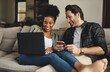 © A. Frank/peopleimages.com - We just share a special connection between us. a happy young couple using a laptop and cellphone while relaxing on a couch home.