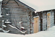 Old rustic house made of timber and covered in snow. The building has yellow or orange wooden doors. Some tools on the side of the wooden house. Snowy village in Lapland, Finland on a cold winter day.