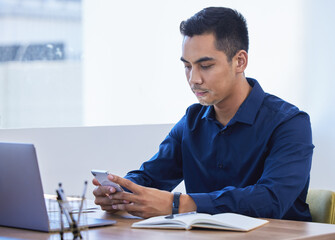 Poster - A few texts just landed in his inbox. a young businessman using a cellphone in an office.