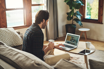 Canvas Print - Let the blogging begin. a handsome young man using his laptop while relaxing on a couch at home.