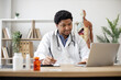 © sofiko14 - Focused african american man with stethoscope typing on laptop and making notes while sitting at writing desk with pill bottles on foreground. Efficient physician analyzing data via net in clinic.