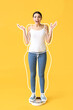 © Pixel-Shot - Surprised young woman after slimming standing on weight scales against yellow background