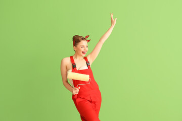 Poster - Young pin-up woman in red uniform with paint roller on green background