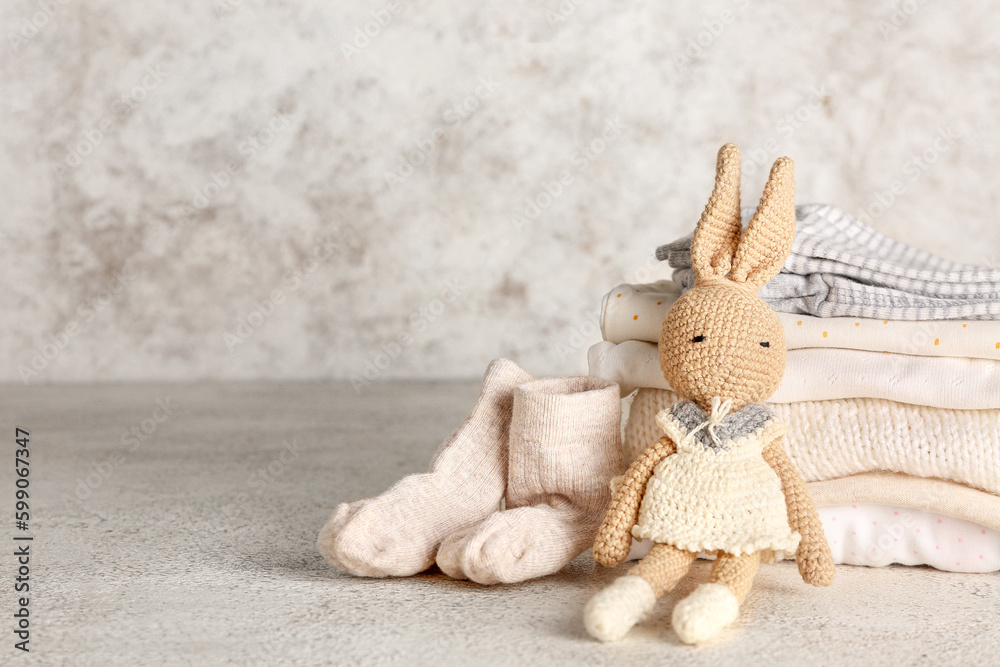 Stack of baby clothes and knitted toy bunny on light background