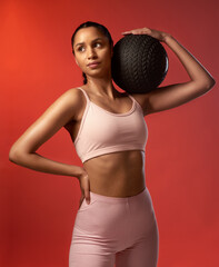 Wall Mural - Focused and ready to smash another session. Studio shot of a sporty young woman holding an exercise ball against a red background.