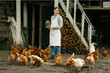 © Dmytro - an attractive young woman standing near the chicken coop holding a jar with grain and feeding the chickens