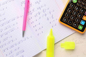 Copybook with maths formulas, calculator and pens on white wooden table