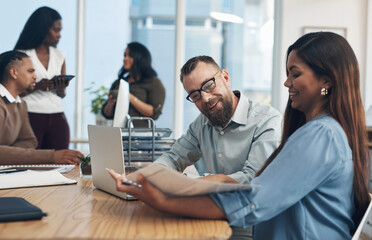 Poster - I had to show you the figures for the month. two young businesspeople sitting together and reading through paperwork while their colleagues work in the background.