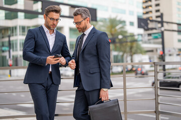 Wall Mural - Business partners talking outdoor. Two businessmen discussing outdoor. Two business people talk project strategy. Two american businessmen in suits walk outdoors in the city and discuss business.