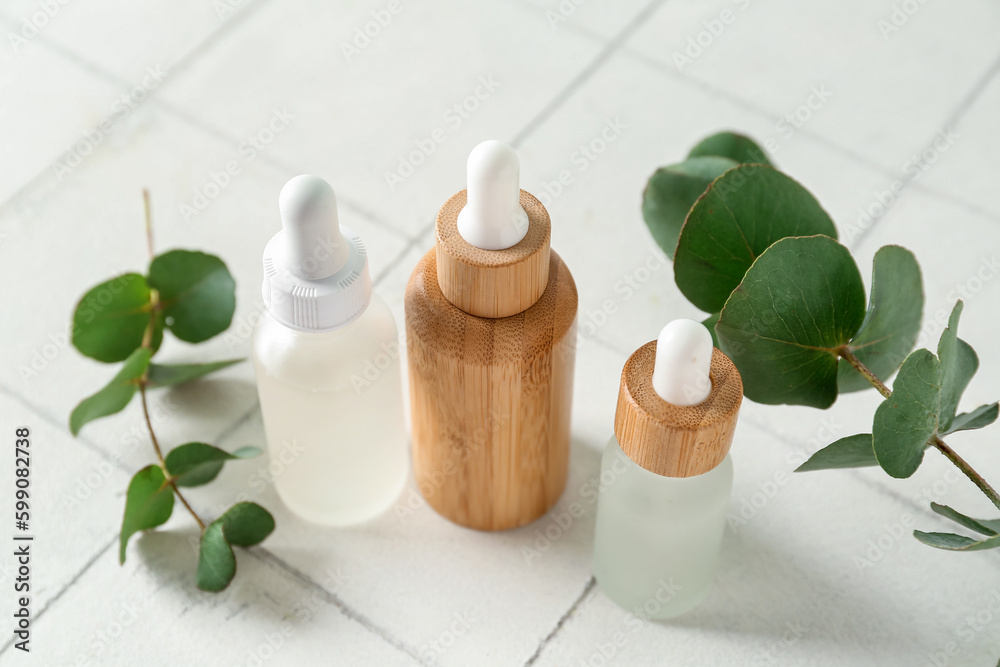 Bottles of cosmetic oil and eucalyptus branches on white tile