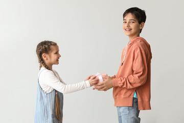 Poster - Little boy greeting his sister with gift on light background. Children's Day celebration