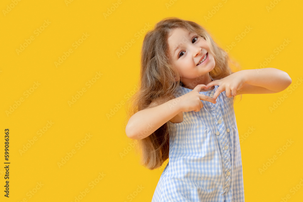 Little girl making heart with her hands on yellow background. Children's Day celebration